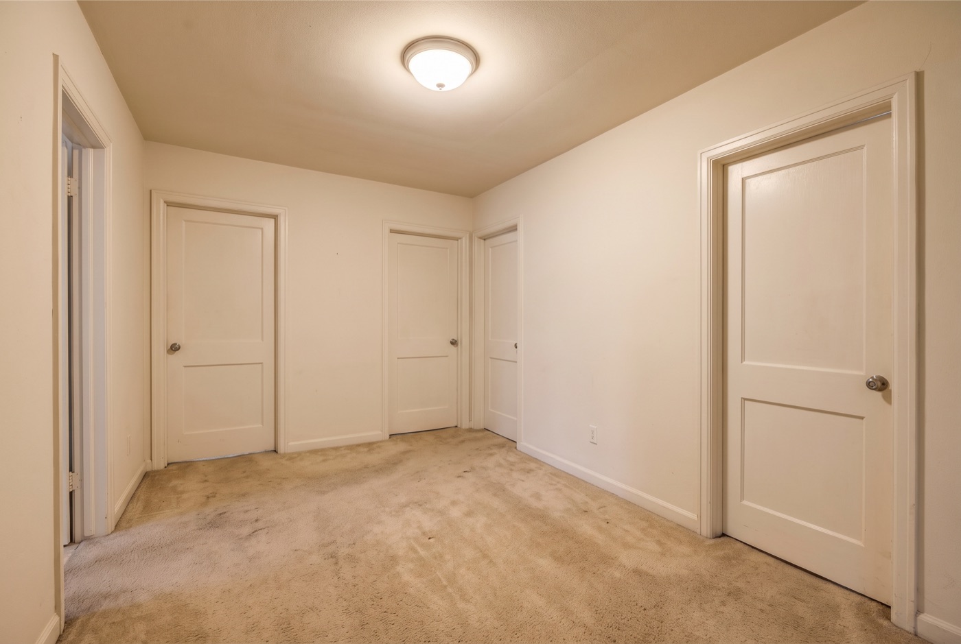 An empty beige upstairs hallway with three closed doors